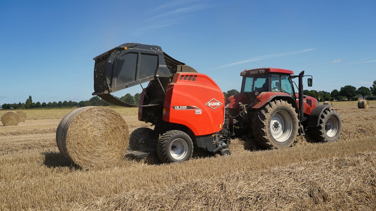Tractor with hay baler operating in a sunny field in Schleswig-Holstein, Germany.