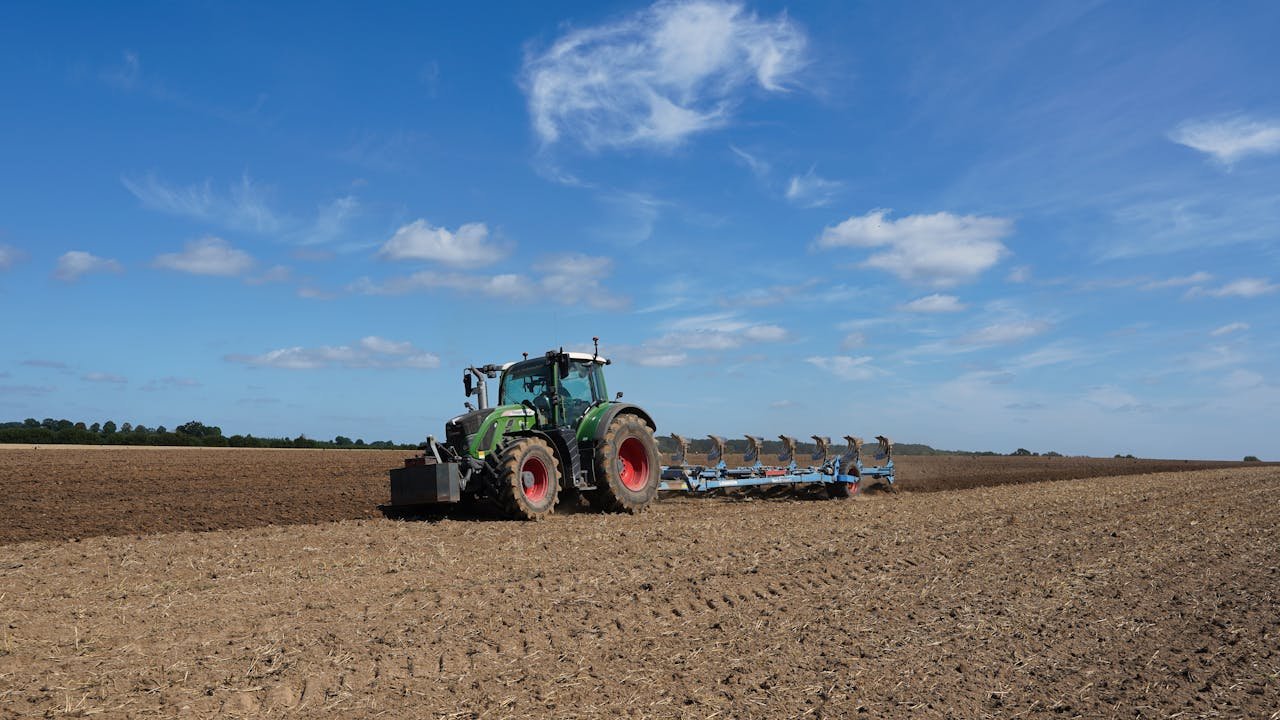Tractor working in a large field under a clear blue sky in Geesthacht, Schleswig-Holstein.